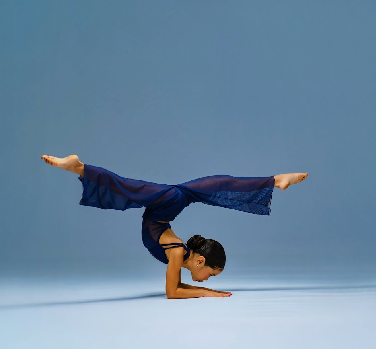 Pichara Luong performing a controlled acrobatic forearm balance in a blue costume